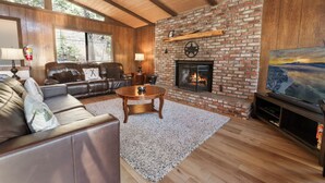 A living room with a brick fireplace, leather sofa, and a flat-screen TV. - Treetop Falls (Big Bear Lake)