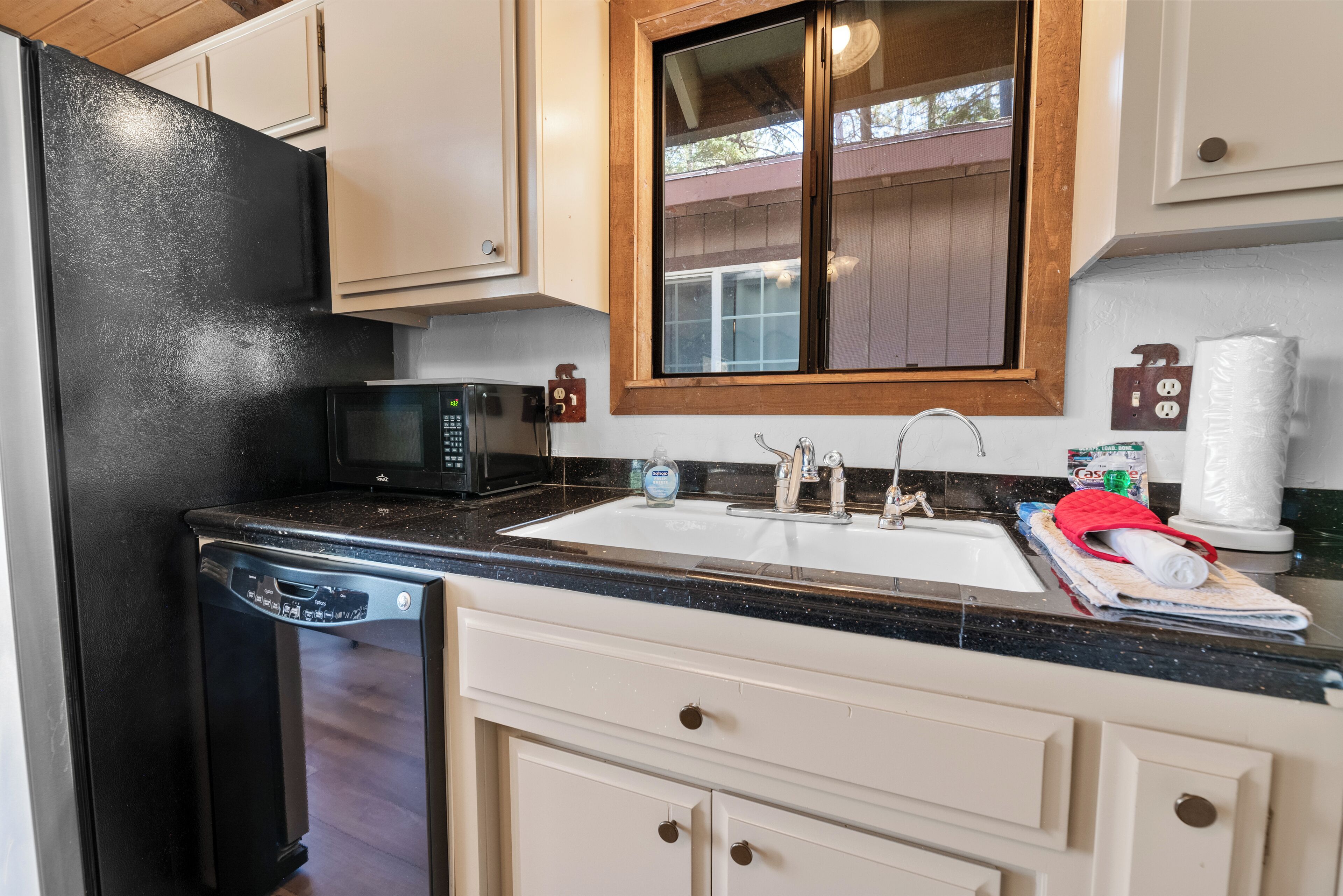 A kitchen with a black refrigerator, a microwave, a sink with a wooden countertop, and white cabinets.