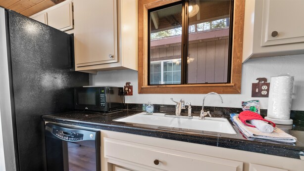 A kitchen with a black refrigerator, a microwave, a sink with a wooden countertop, and white cabinets. - Treetop Falls (Big Bear Lake)