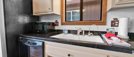 A kitchen with a black refrigerator, a microwave, a sink with a wooden countertop, and white cabinets.