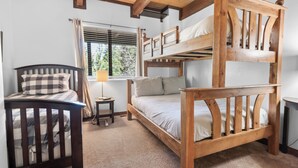 A bunk bed room with a wooden headboard, a bedside table with a lamp, and a window with blinds. - Treetop Falls (Big Bear Lake)