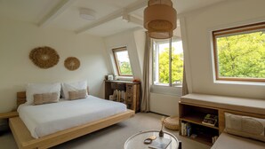 A bedroom with a wooden bed, a small round table, a bookshelf, and large windows with a view of trees. - Canal View Stay Amsterdam (Amsterdam)