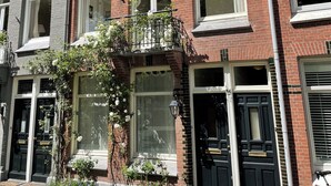 A row of red brick townhouses with large windows, a black bicycle parked outside, and a small garden area with flowers. - Canal View Stay Amsterdam (Amsterdam)