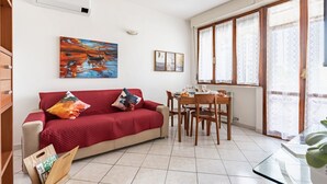 Ein Wohnzimmer mit einem roten Sofa, einem Esstisch und einem großen Fenster mit gemusterten Vorhängen.