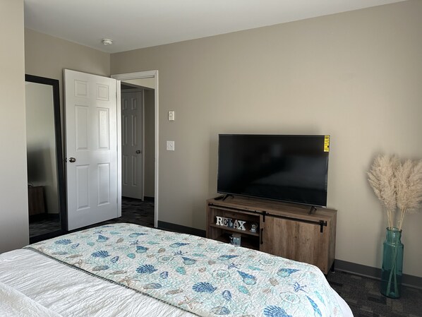 A hotel room with a bed, a television on a wooden stand, a door, and a vase with dried plants. - The Hidden Oasis, Duplex A. Close to almost everything! (Enfield)