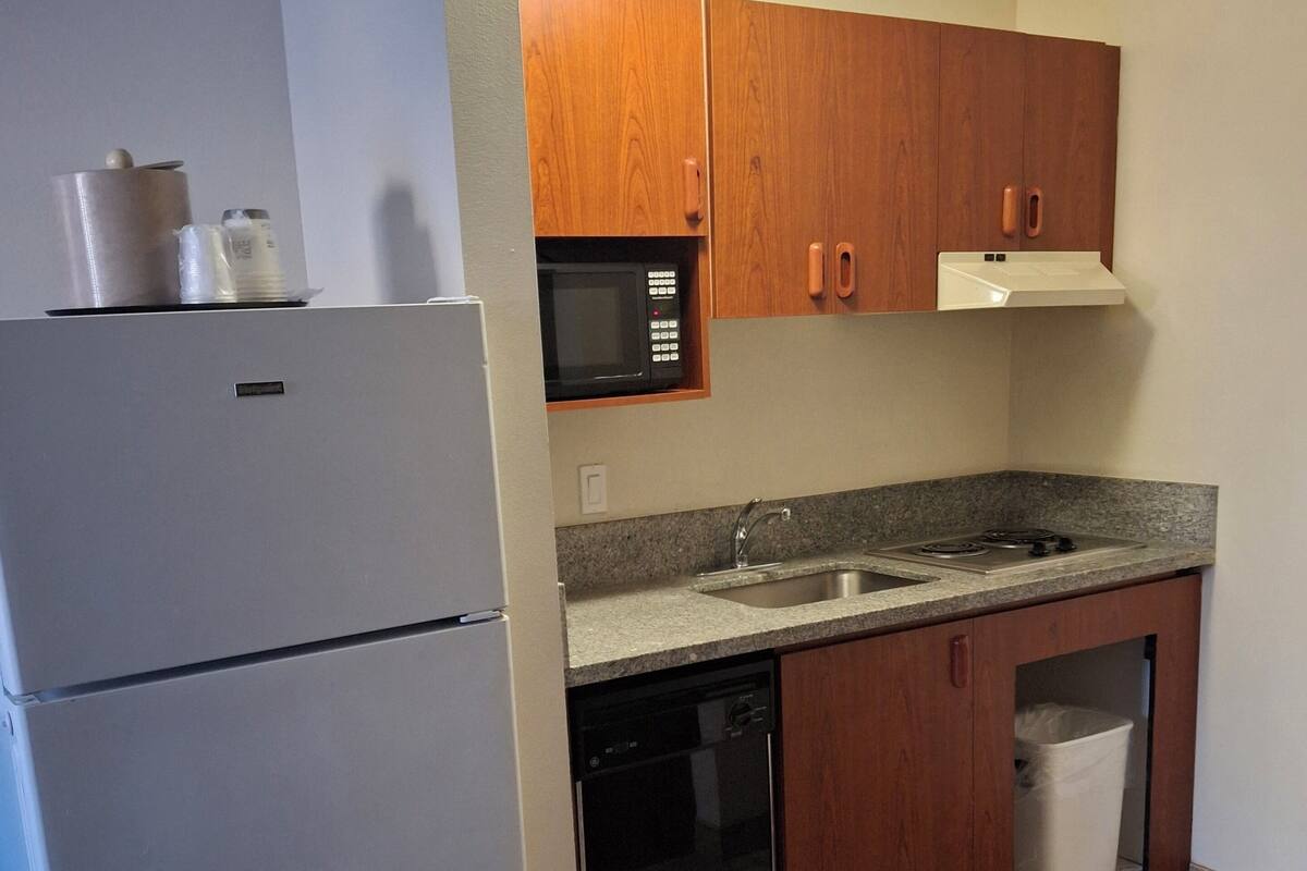 A compact kitchen with a refrigerator, microwave, dishwasher, and wooden cabinets.