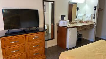 Habitación de hotel con tocador de madera, televisor, refrigerador pequeño, lavamanos con espejo y cama con cubrecama amarillo.