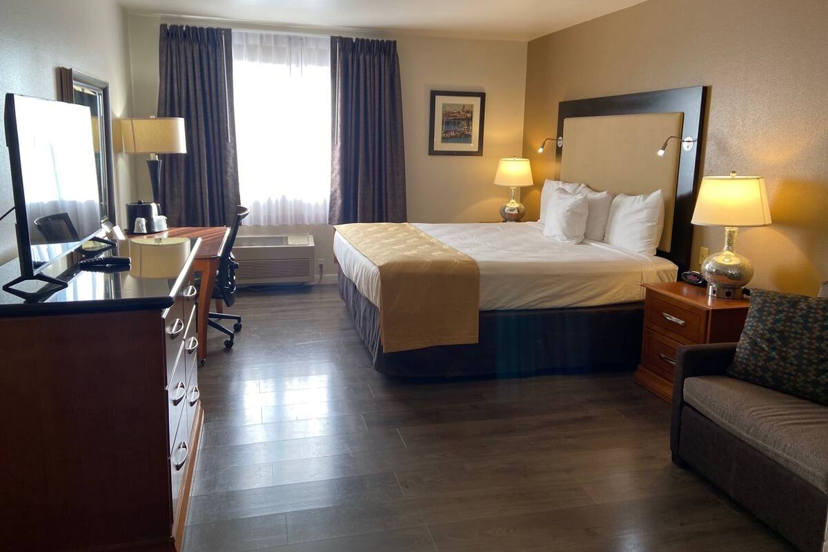 A hotel room with a bed, desk, chair, and two bedside lamps.