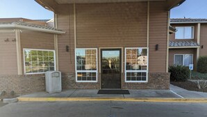 A building with a brick facade, a metal awning, and a parking lot with a blue arrow indicating direction.