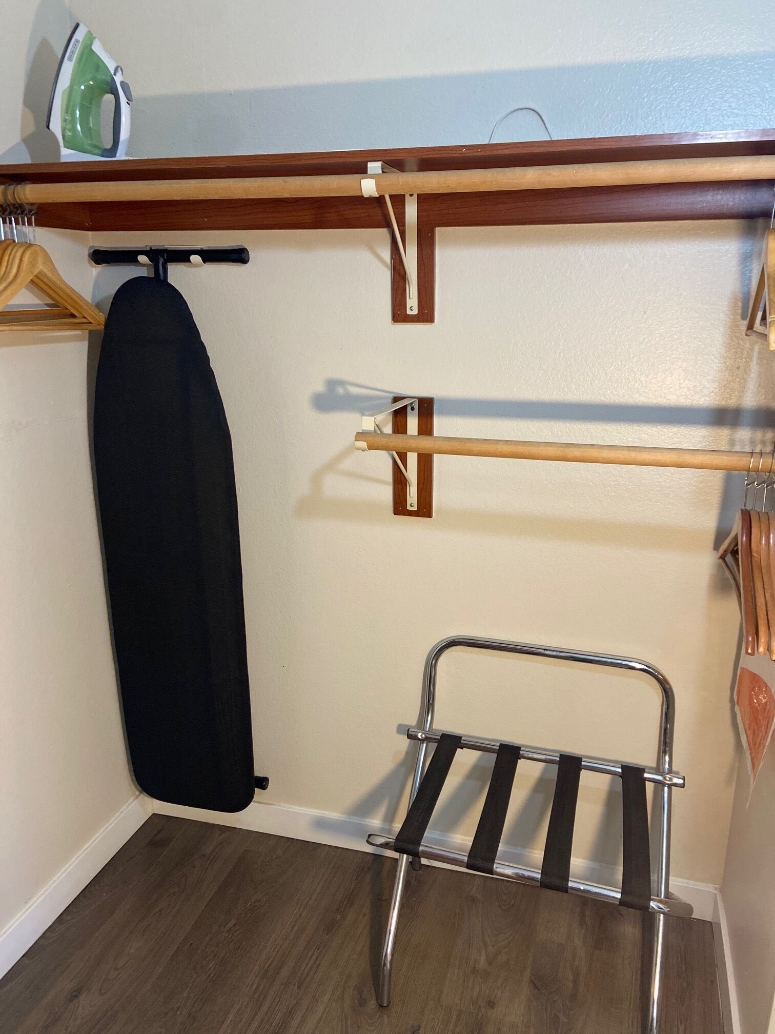 Un rincón de una habitación con una estantería de madera, un perchero y un tendedero de metal.