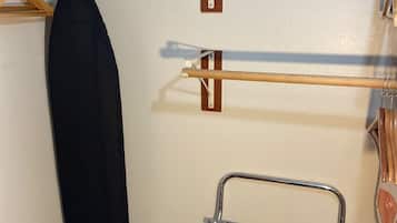 A corner of a room with a wooden shelf, a hanging rack, and a metal drying rack.