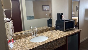 A bathroom with a granite countertop sink, two faucets, a coffee maker, and a microwave. - Toppenish Inn and Suites (Toppenish)