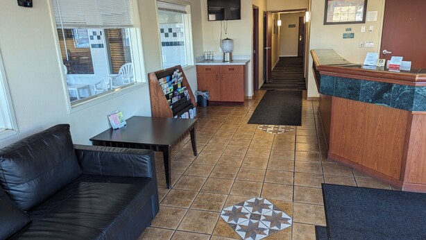 A hotel lobby with a reception desk, a seating area with a couch and a table, a bulletin board, and a tiled floor. - Toppenish Inn and Suites (Toppenish)
