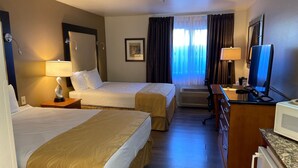 A hotel room with two beds, a desk with a computer, a TV, and a window with curtains.