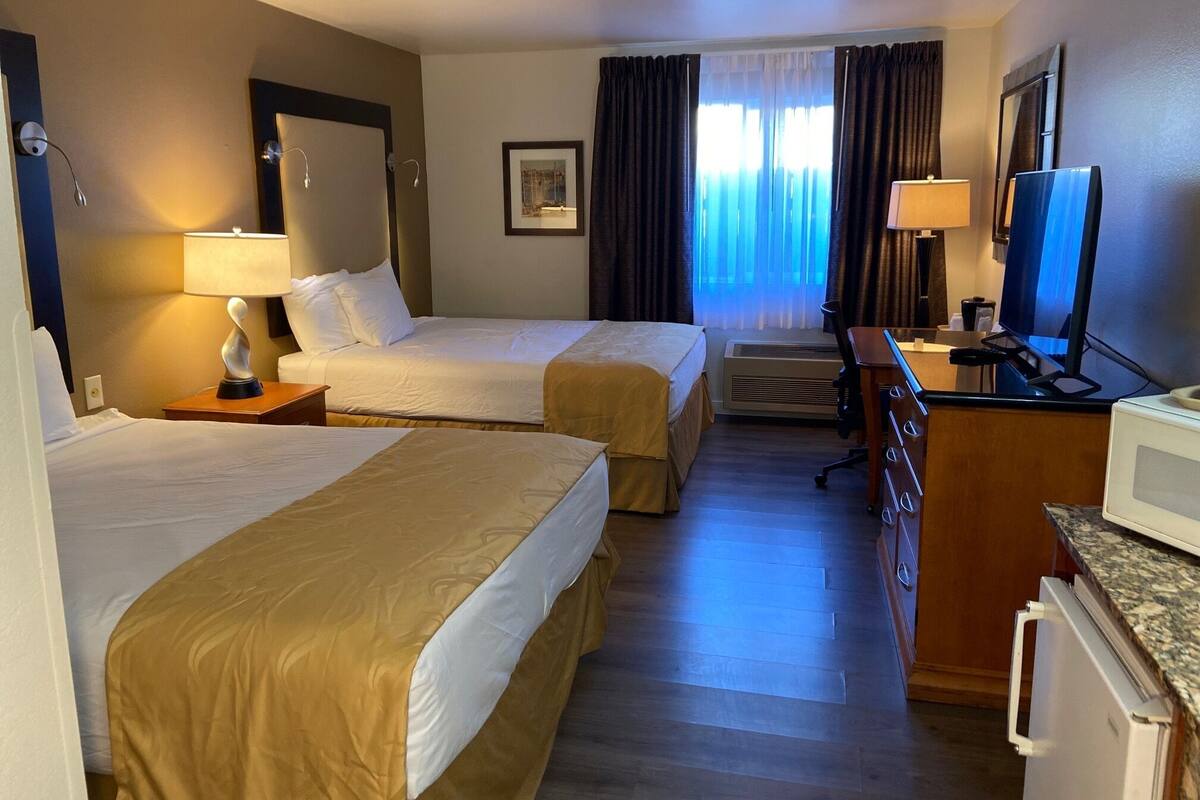 A hotel room with two beds, a desk with a computer, a TV, and a window with curtains.