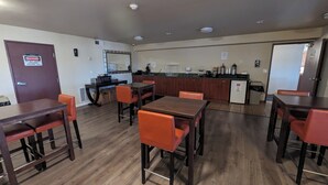 A dining area with wooden tables and orange chairs, a kitchen area with a refrigerator and coffee machine, and a door marked "Danger" indicating restricted access. - Toppenish Inn and Suites (Toppenish)
