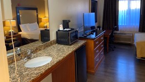 A hotel room with a bed, a desk with a computer, a coffee maker, a TV, and a bathroom with a sink and mirror. - Toppenish Inn and Suites (Toppenish)