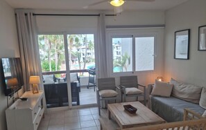 A hotel room with a TV, a desk, a sofa, and a balcony with a pool view.
