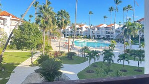 A resort with a swimming pool, palm trees, and white buildings with red roofs. - I 203, Stanza Mare, 2 bed, Private Beach, Bavaro , Punta Cana, 24 hrs security
 (Bavaro)