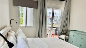A hotel room with a bed, a desk, and a view of a pool and buildings. - I 203, Stanza Mare, 2 bed, Private Beach, Bavaro , Punta Cana, 24 hrs security
 (Bavaro)