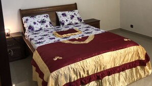 Een netjes opgemaakt bed met een bloemendecor en twee passende kussens, een houten hoofdbord en een nachtkastje met een lamp.