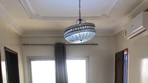 Een kamer met een groot raam, een hanglamp, een stoel en een blauwe mand op de vloer.