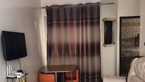 Een woonkamer met een bank, een tafel, een televisie en een gordijn.