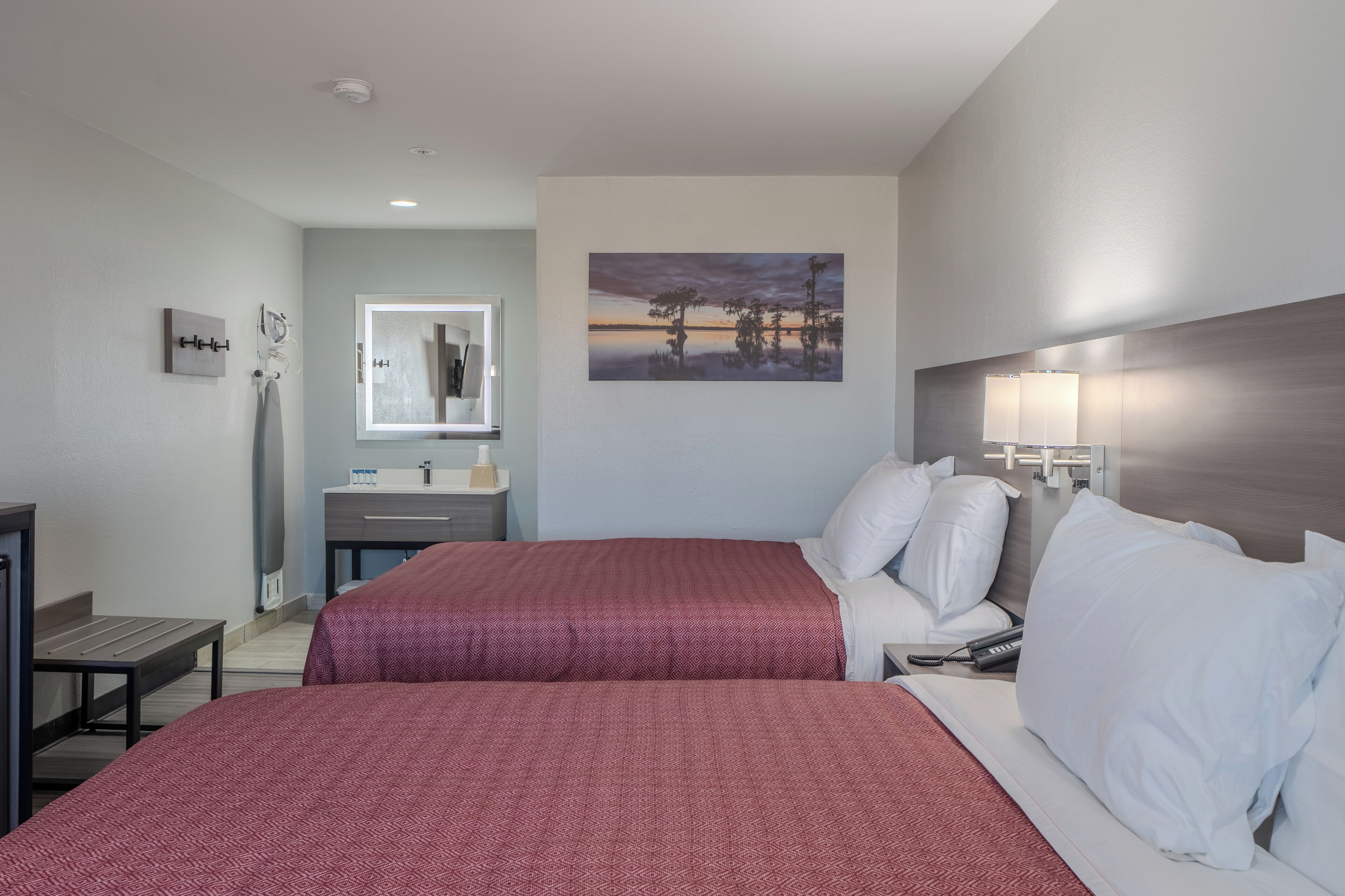A hotel room with two beds, a bathroom, and a painting on the wall.