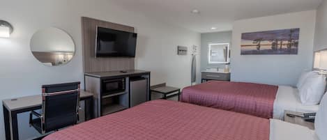 Habitación de hotel con dos camas, un escritorio, un televisor de pantalla plana, un microondas, una mesita y una silla.