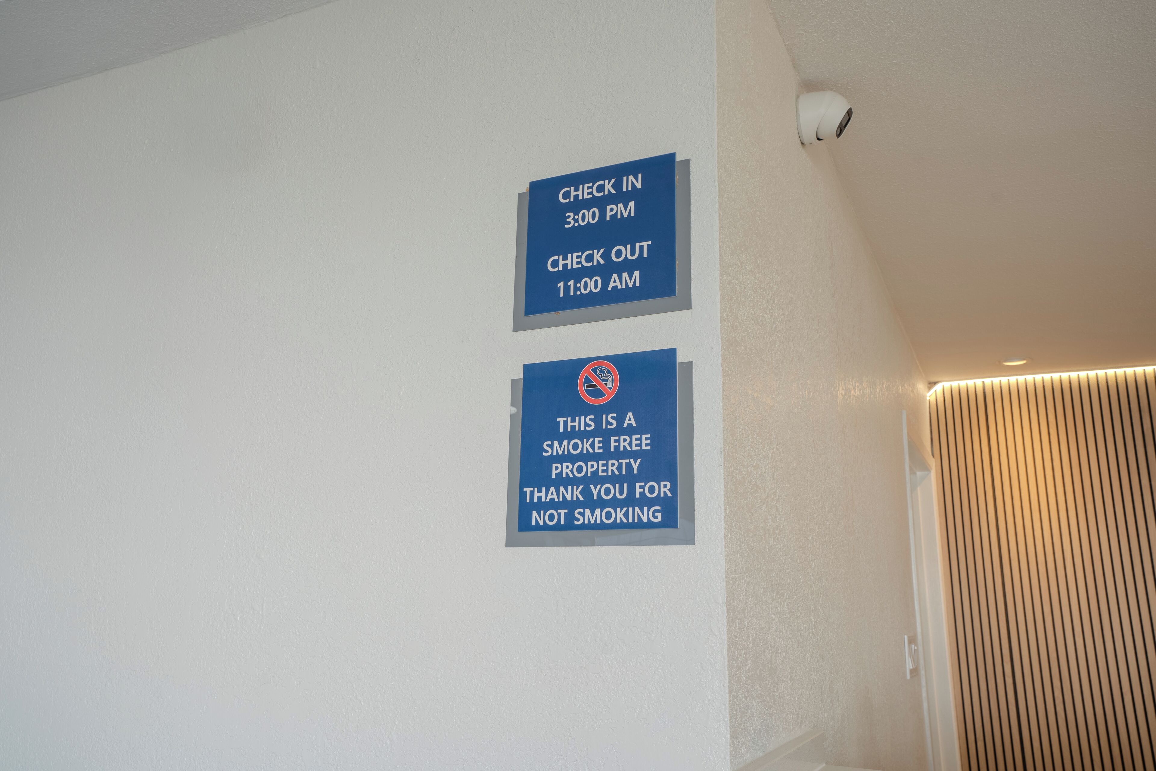 Eine Wand mit zwei Schildern: eines zeigt die Check-in-Zeit um 15:00 Uhr und die Check-out-Zeit um 11:00 Uhr an, das andere kennzeichnet das Hotel als Nichtraucherzone.