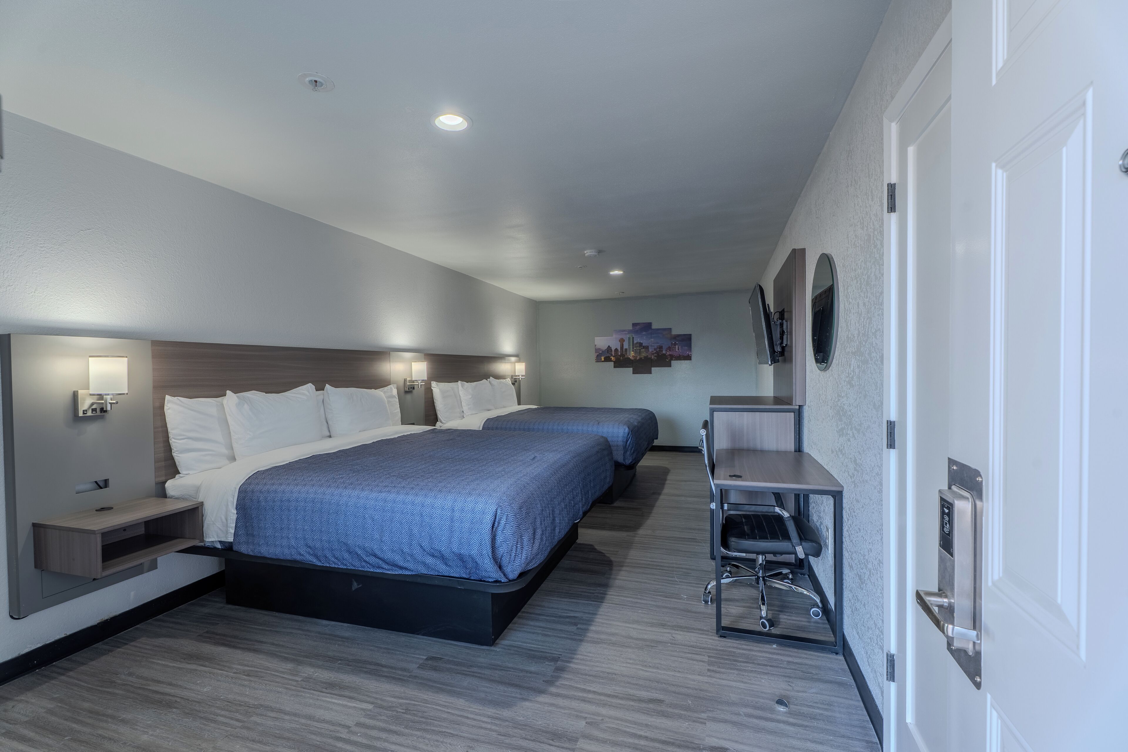 A modern hotel room with two beds, a desk, and a chair.