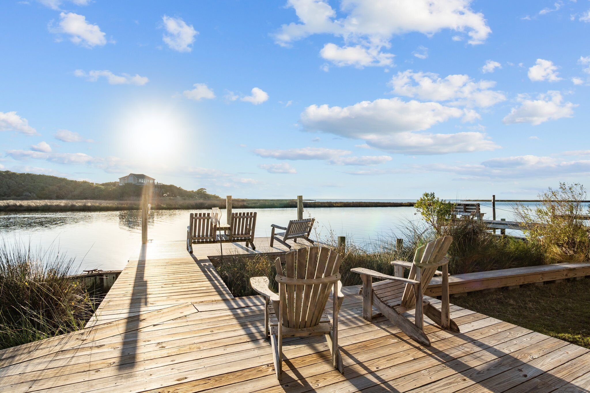 Eine Holzterrasse mit Adirondack-Stühlen mit Blick auf einen ruhigen See, im Hintergrund ein Hügel und ein klarer Himmel.