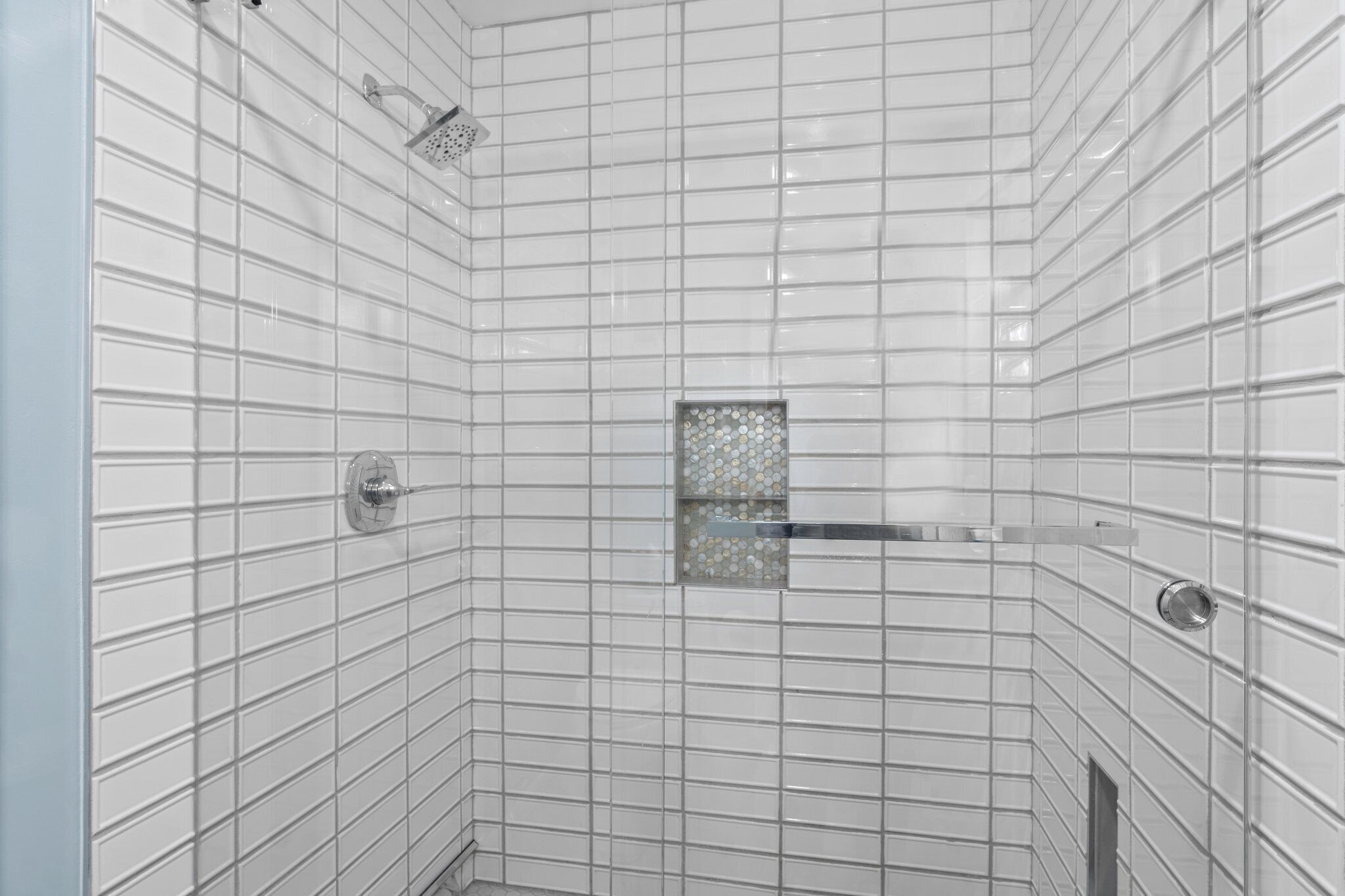 Eine geflieste Dusche mit Handbrause und einem in einer Eckausführung angebrachten Waschbecken mit Glasabdeckung.