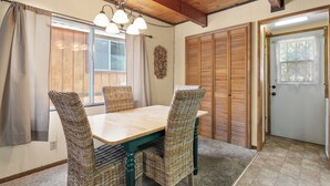 A dining area with a wooden table and wicker chairs, a ceiling with exposed beams, and a door with a window. - Cabin in the Pines (Big Bear Lake)