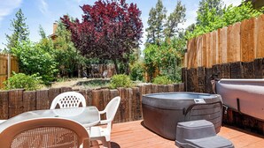 An outdoor patio area with a hot tub, a table with chairs, and a wooden fence. - Cabin in the Pines (Big Bear Lake)