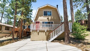A cabin with a wooden deck, a red door, and a staircase leading to a balcony. - Cabin in the Pines (Big Bear Lake)