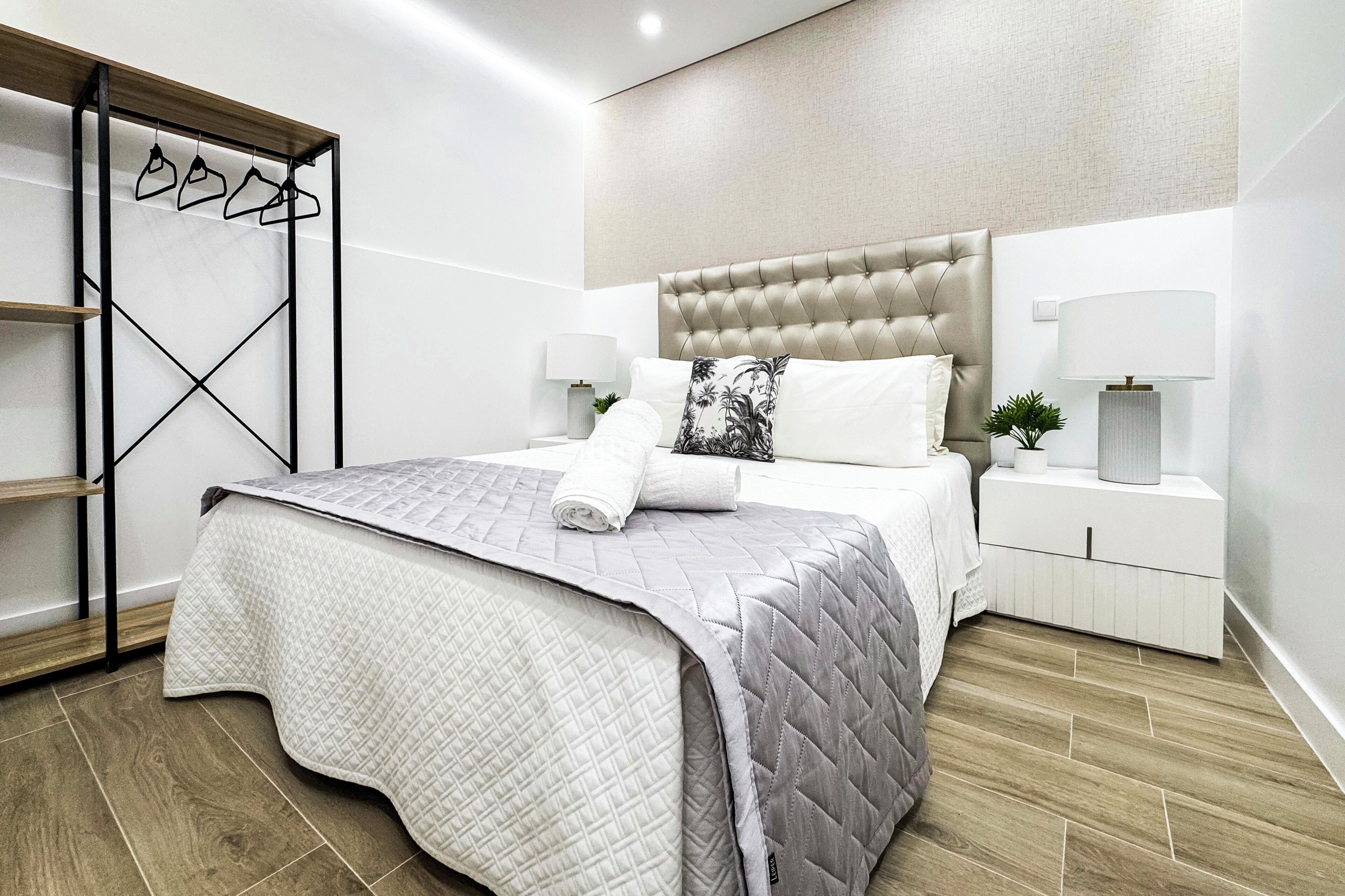 A neatly arranged bedroom with a bed, nightstands, a wall-mounted shelf, and a hanging shoe rack.
