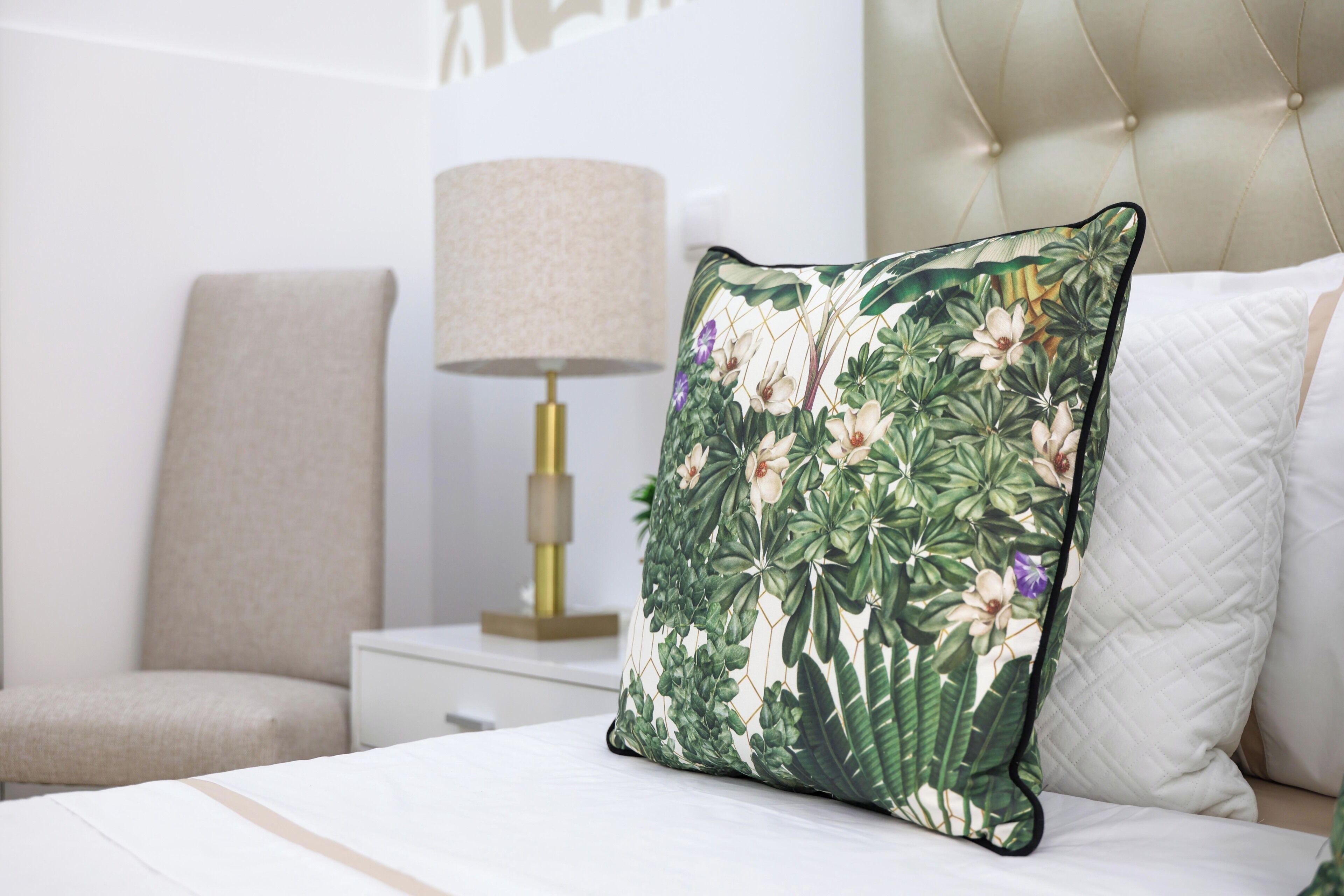 Un lit avec un coussin à motifs floraux, une lampe de chevet et une chaise dans une chambre d’hôtel.