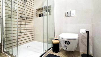 Une salle de bain moderne dotée d’une douche à parois de verre, de toilettes et d’un porte-serviettes.