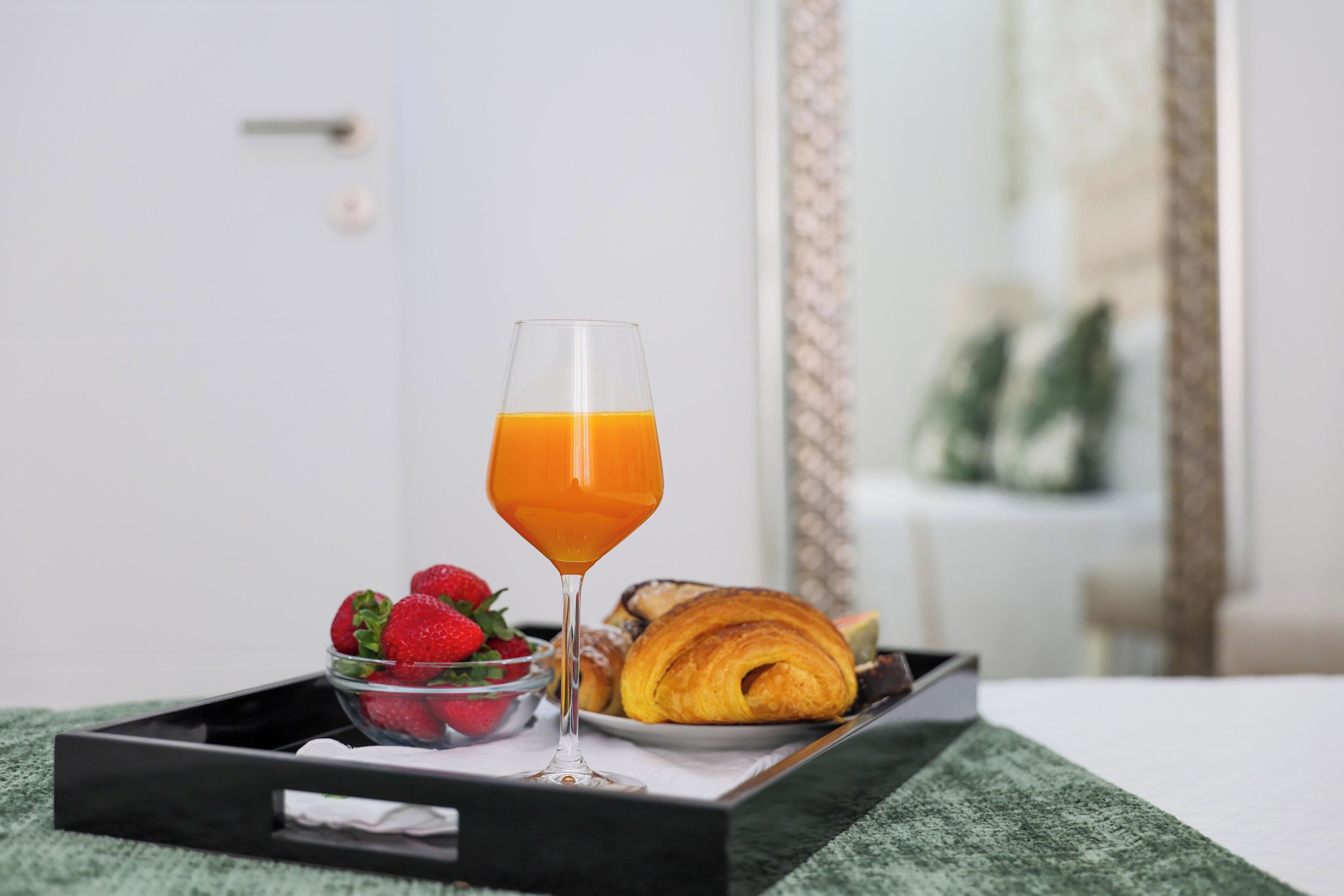 En bakke med morgenmad, appelsinjuice, jordbær og en croissant på en seng.
