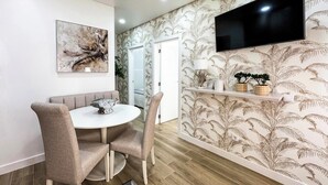 A dining area with a round table, chairs, a painting, a TV, and a patterned wallpaper.