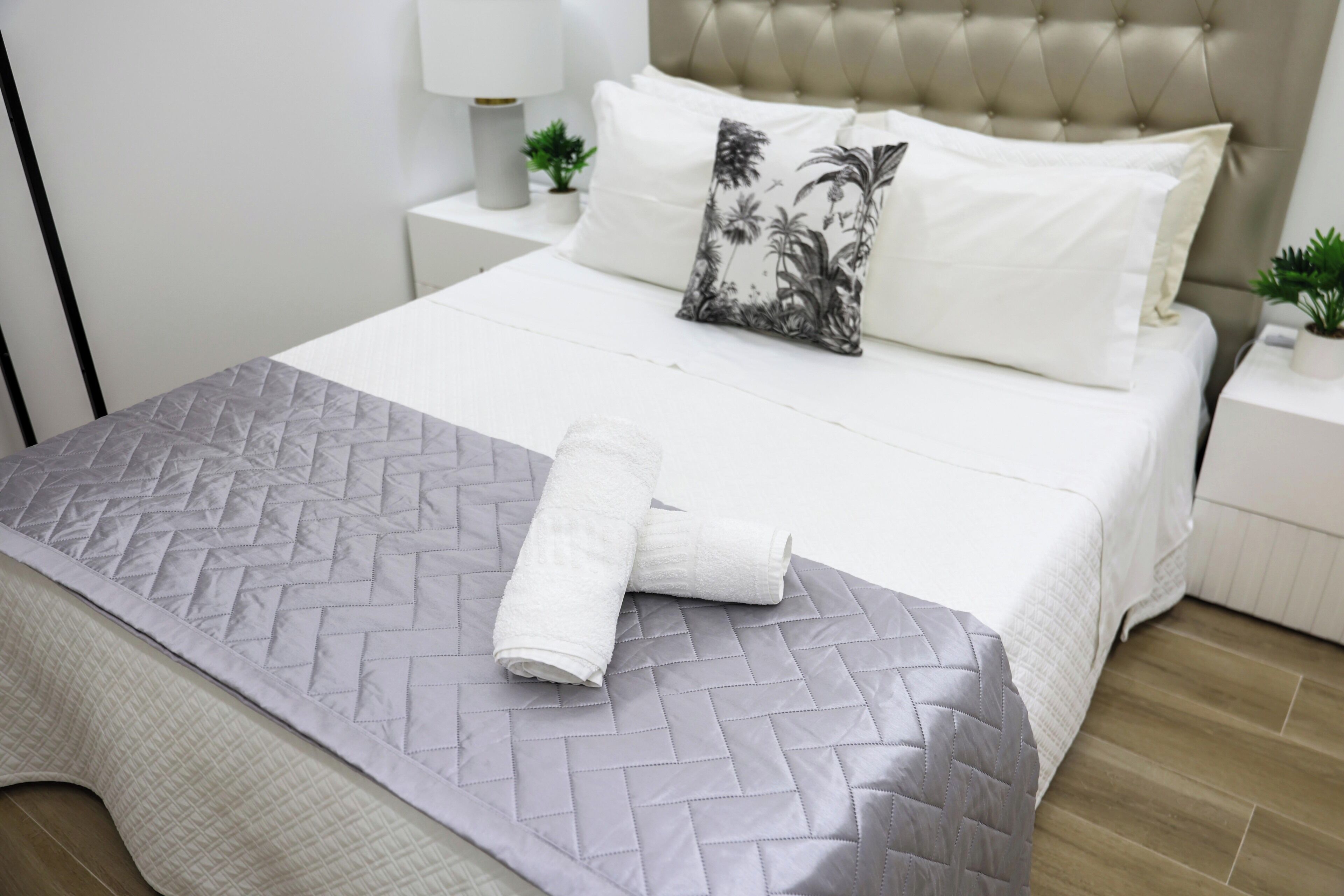 Un lit bien fait, recouvert d’une courtepointe matelassée, avec un oreiller à motifs tropicaux et deux serviettes enroulées posées sur le lit.