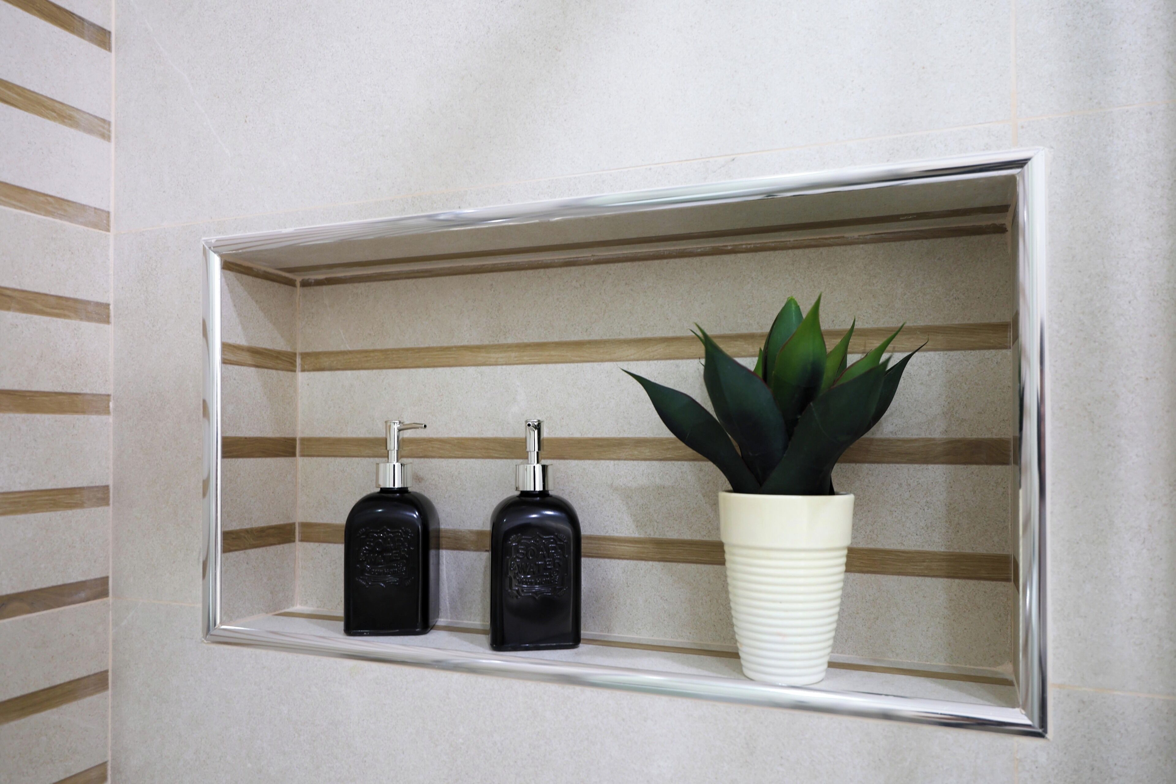 A bathroom shelf with two black soap dispensers and a white vase with a green plant.