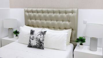 A neatly made bed with a tufted headboard, white bedding, and a decorative pillow. There are two bedside tables with lamps and small potted plants.