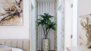 A hallway with a potted plant, a white door, and a wall-mounted artwork.