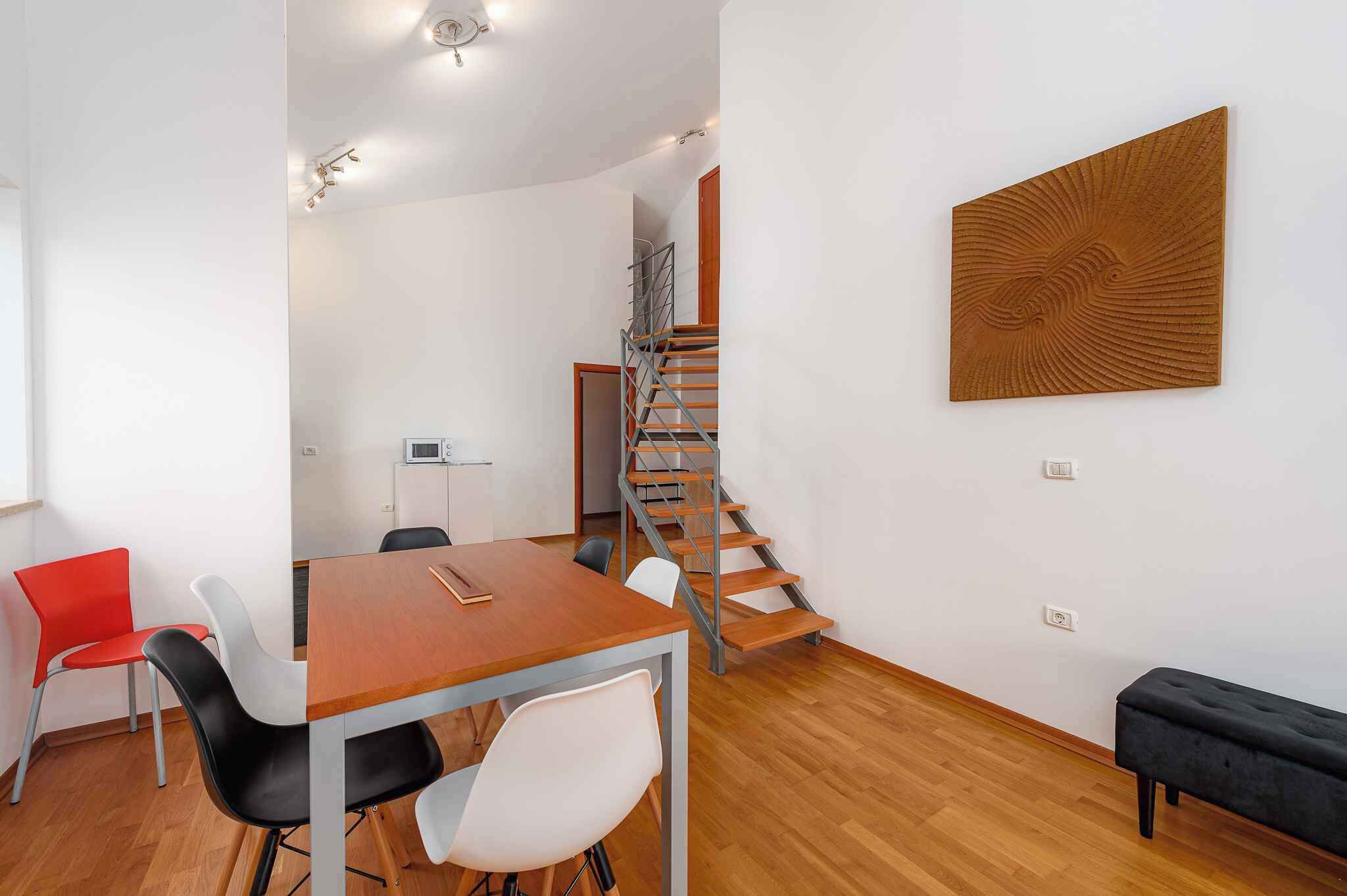 Een moderne kamer met een houten trap, een eettafel met stoelen en een zwarte bank.
