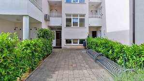 Un immeuble résidentiel à plusieurs étages, doté de balcons, d’une entrée principale et d’un trottoir dallé.