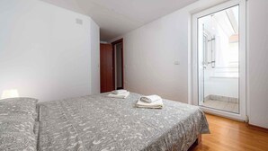 Une chambre à coucher comprenant un lit, une porte et une porte-fenêtre coulissante donnant sur un balcon.