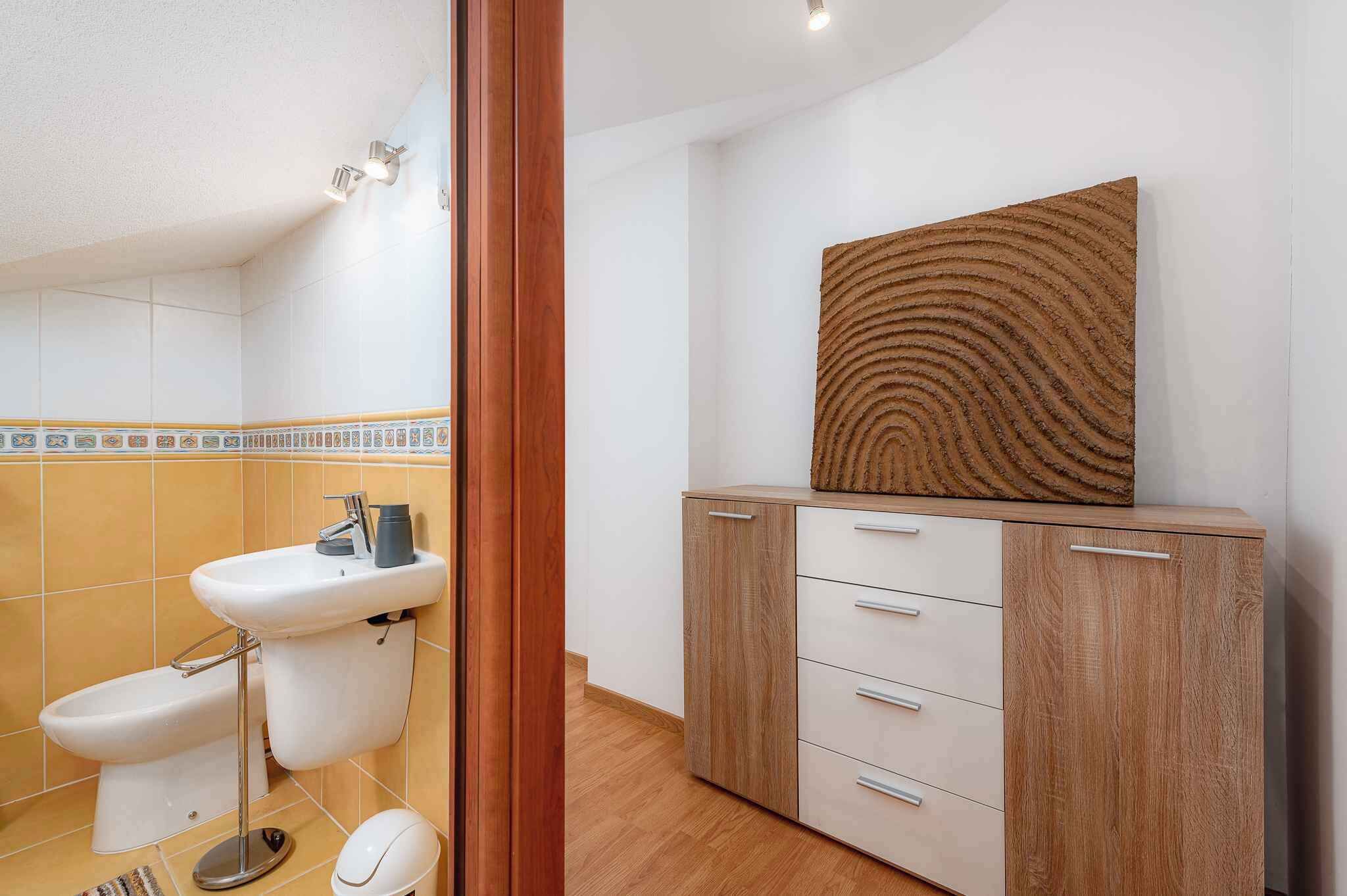 Une salle de bain équipée de toilettes, d’un lavabo, d’un meuble de rangement et d’une œuvre d’art accrochée au mur.