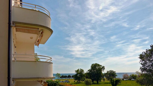 Un immeuble à plusieurs étages doté de balcons donnant sur un espace paysager agrémenté d’arbres et offrant une vue sur la mer.